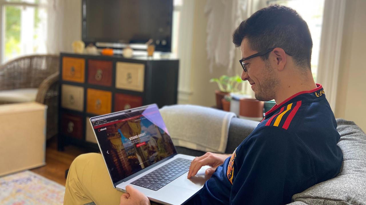 A young man sits smiling with a laptop showing eCornell's homescreen.